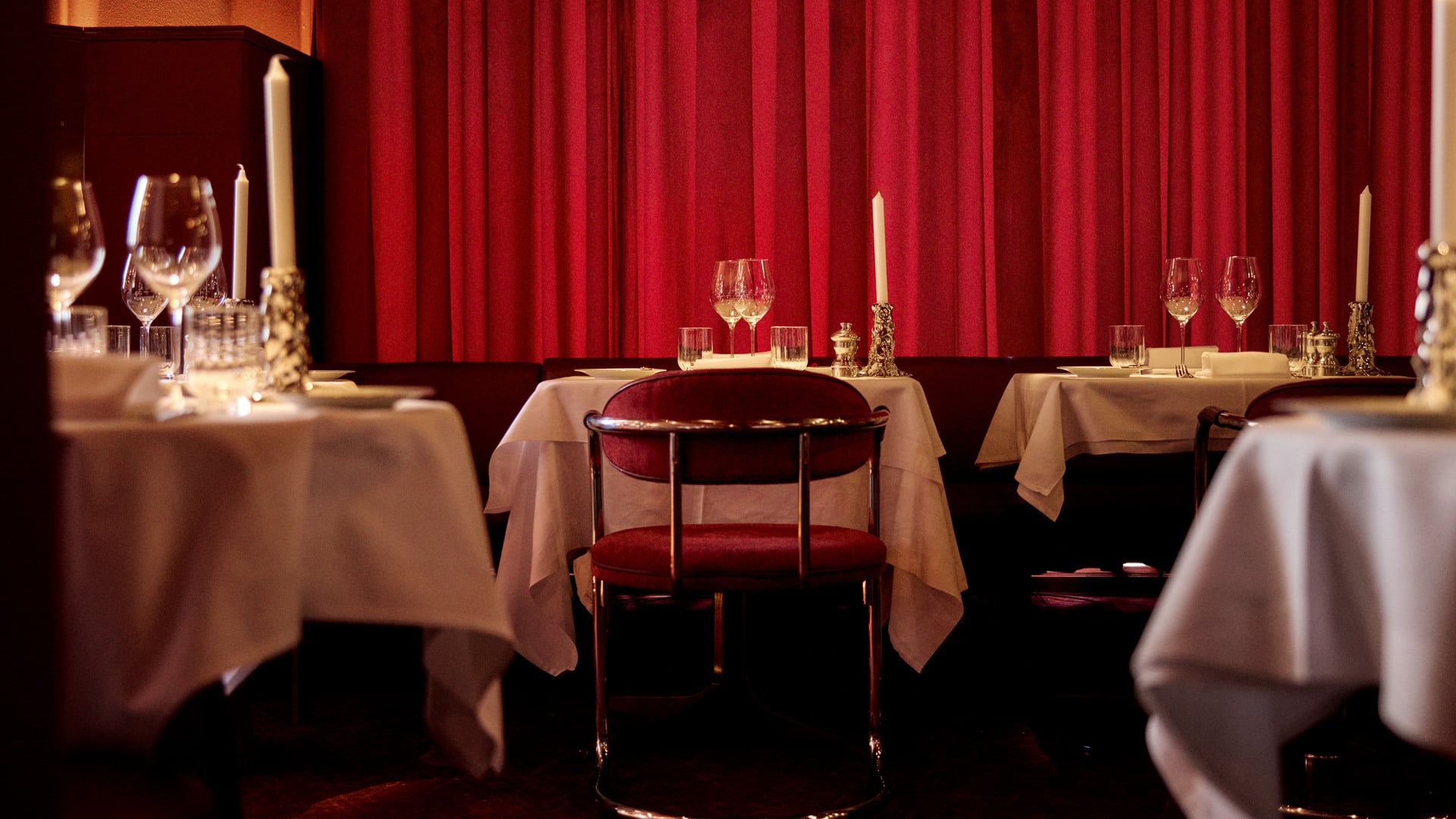 Dukade restaurangbord framför röda sammetsgardiner.