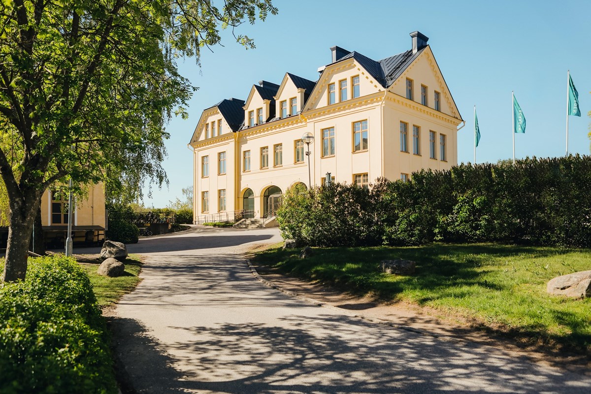 Fastigheten sedd från entrésidan med gångväg och grönska.